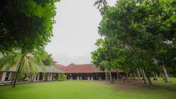 A courtyard with a red-tiled roof building, surrounded by lush green trees and a well-maintained lawn.