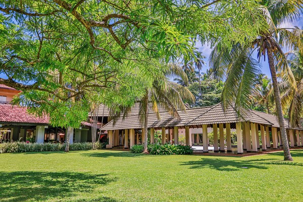 A resort with a covered outdoor area, palm trees, and a well-maintained lawn. - The Palms (Beruwala)