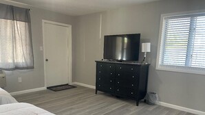 Ein Schlafzimmer mit einem Bett, einem Schminktisch, einem Fernseher und einem Fenster mit Jalousien.