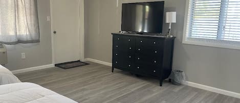 A bedroom with a bed, a dresser, a TV, and a window with blinds.