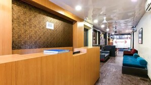 A reception area with a wooden reception desk, a blue sofa, and a wall-mounted sign. - Hotel Red Palm (Mumbai)