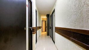 A hallway with doors on both sides, a tiled floor, and a textured wall. - Hotel Red Palm (Mumbai)