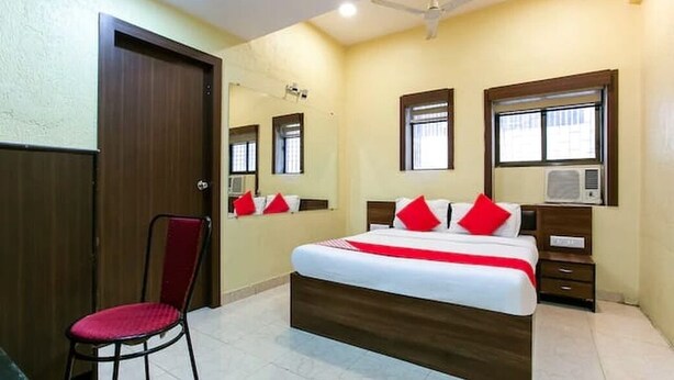 A hotel room with a bed, a chair, a desk, a mirror, and a ceiling fan. - Hotel Red Palm (Mumbai)