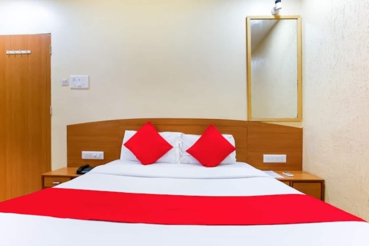 Hotellihuone, jossa on puinen sängynpääty, valkoisilla lakanoiden ja punaisten tyynyjen koristeltu sänky, punainen heittopeitto, yöpöytä, jossa on puhelin, ja seinällä oleva peili.