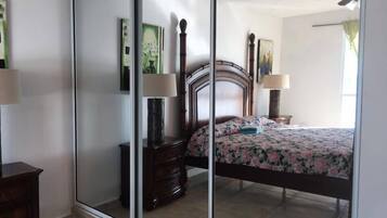 A bedroom with a large mirror, a wooden bed frame, a floral bedspread, and a nightstand with a lamp.