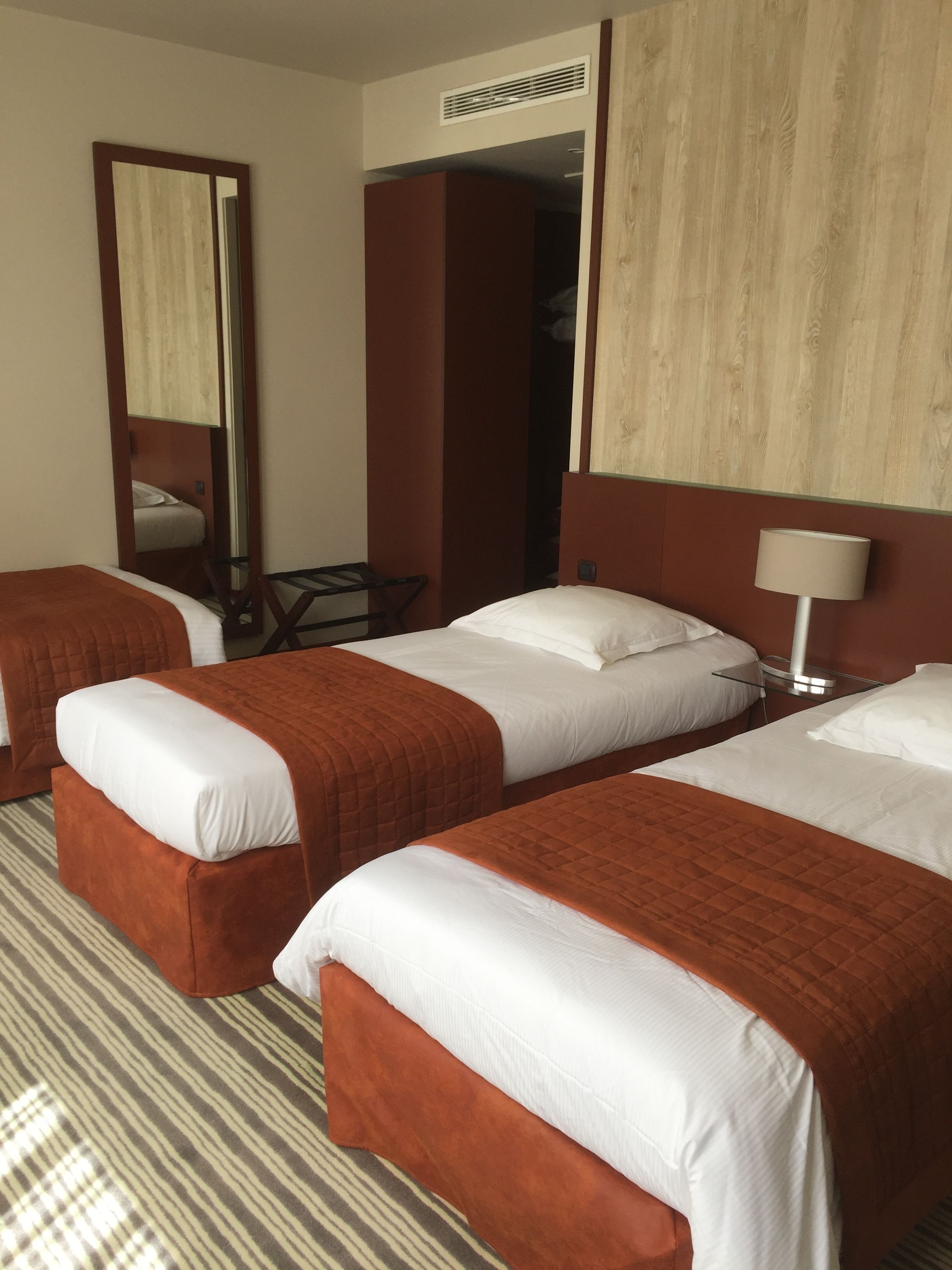 A hotel room with three beds, a mirror, a desk, and a lamp.