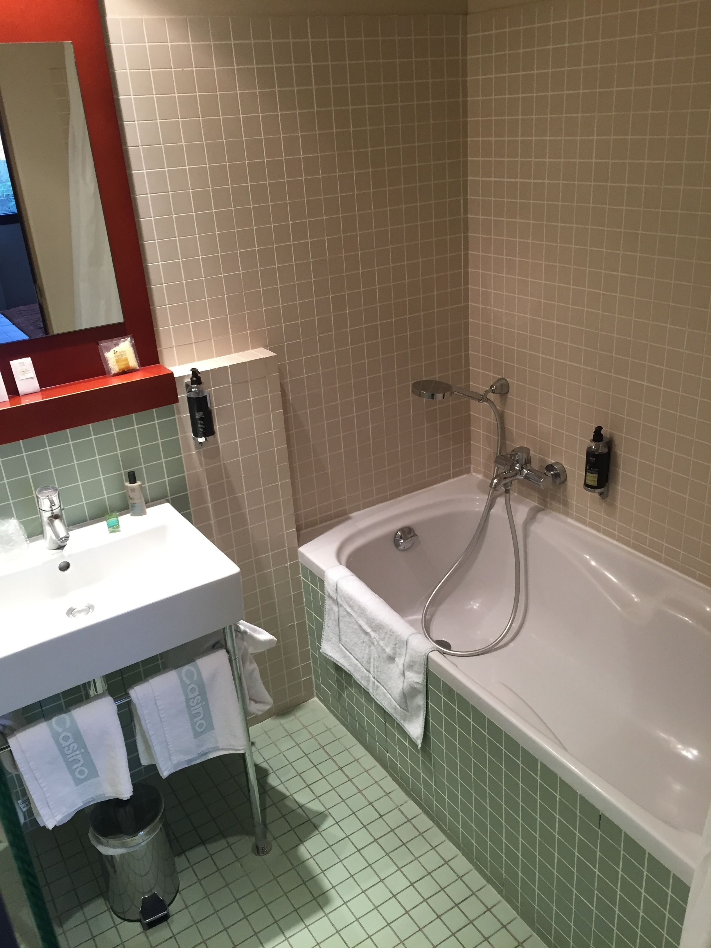 A bathroom with a white sink, a mirror, a bathtub, and green-tiled walls.