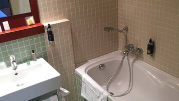 A bathroom with a white sink, a mirror, a bathtub, and green-tiled walls.