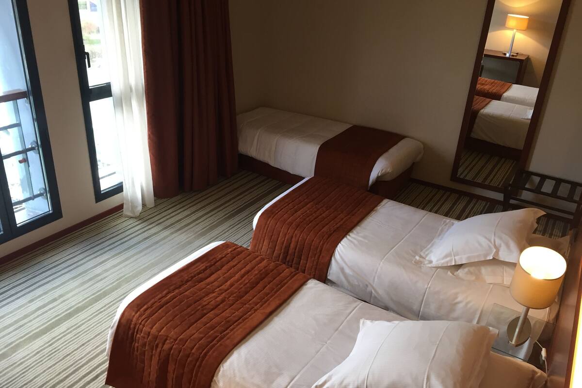 A hotel room with two beds, a large window, and a mirror.
