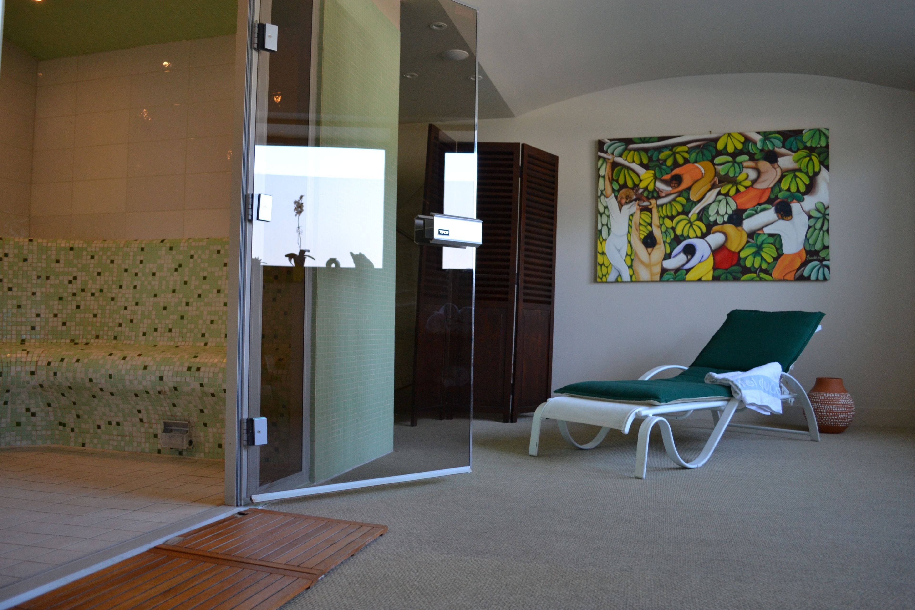 Una habitación con puerta de vidrio que da a un baño, un sillón verde y un cuadro llamativo en la pared.