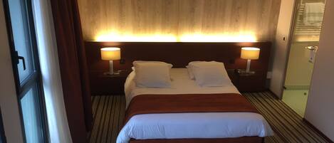 Une chambre d’hôtel avec un grand lit, deux lampes de chevet, une tête de lit en bois et une moquette à rayures.