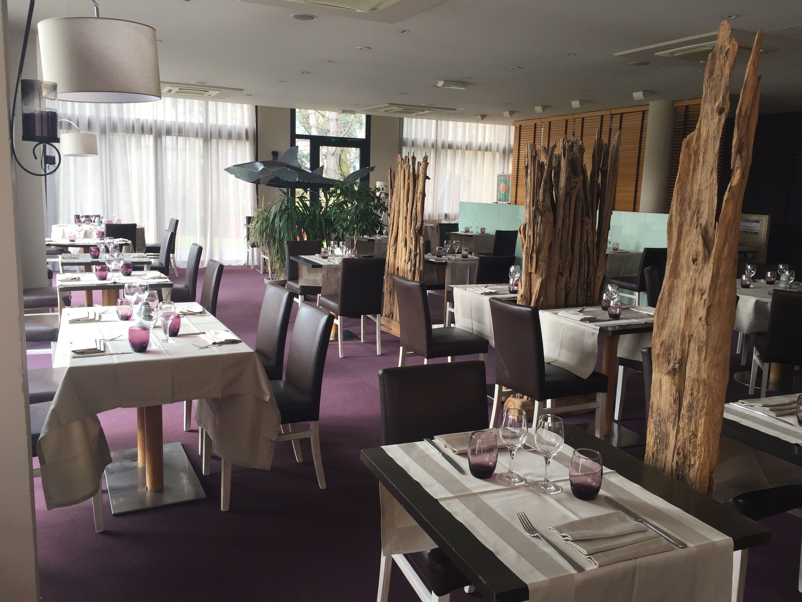 A restaurant with tables set for dining, featuring a modern interior with wooden accents and a large window providing natural light.