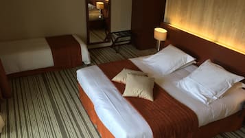 Ett hotellrum med två separata sängar, en stor spegel, ett nattduksbord med en lampa och en randig matta.