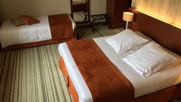 A hotel room with two beds, each with white linens and brown headboards. There is a small table with a lamp and a mirror on the wall.