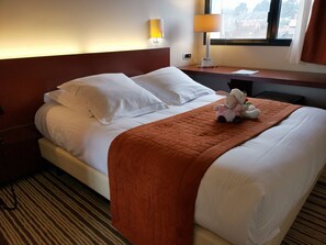 Une chambre d’hôtel avec un lit, des oreillers, une couverture, une lampe et une fenêtre.