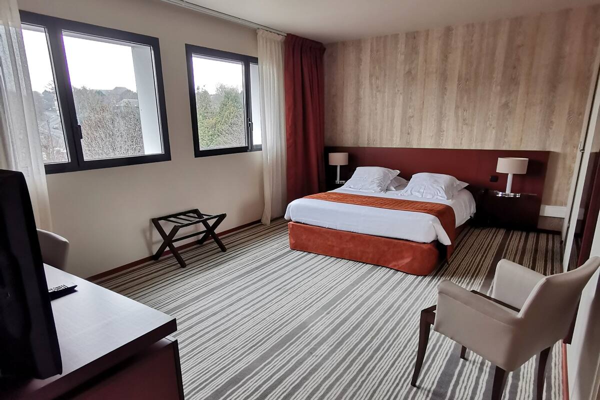 A hotel room with a bed, a desk, a chair, and a TV.