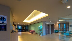 Eine moderne Lobby mit einer Rezeption, einer Glastheke, einem violetten Sofa und einer Deckenleuchte.
