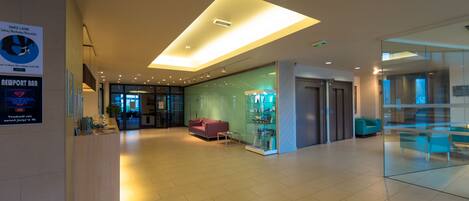 A modern lobby with a reception desk, a glass display case, a purple sofa, and a ceiling light fixture.