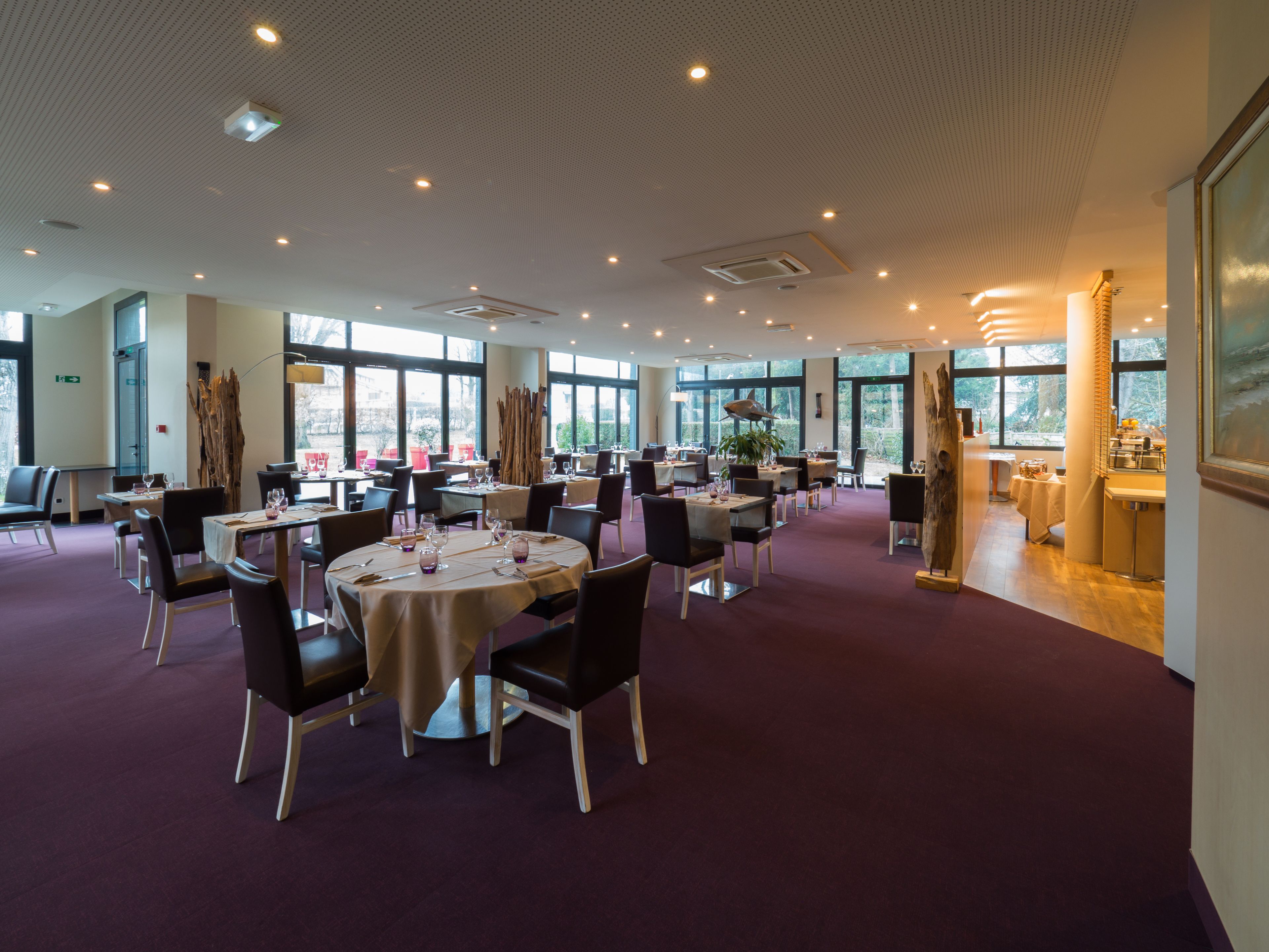 A spacious dining area with round tables, chairs, and a high ceiling with recessed lighting.