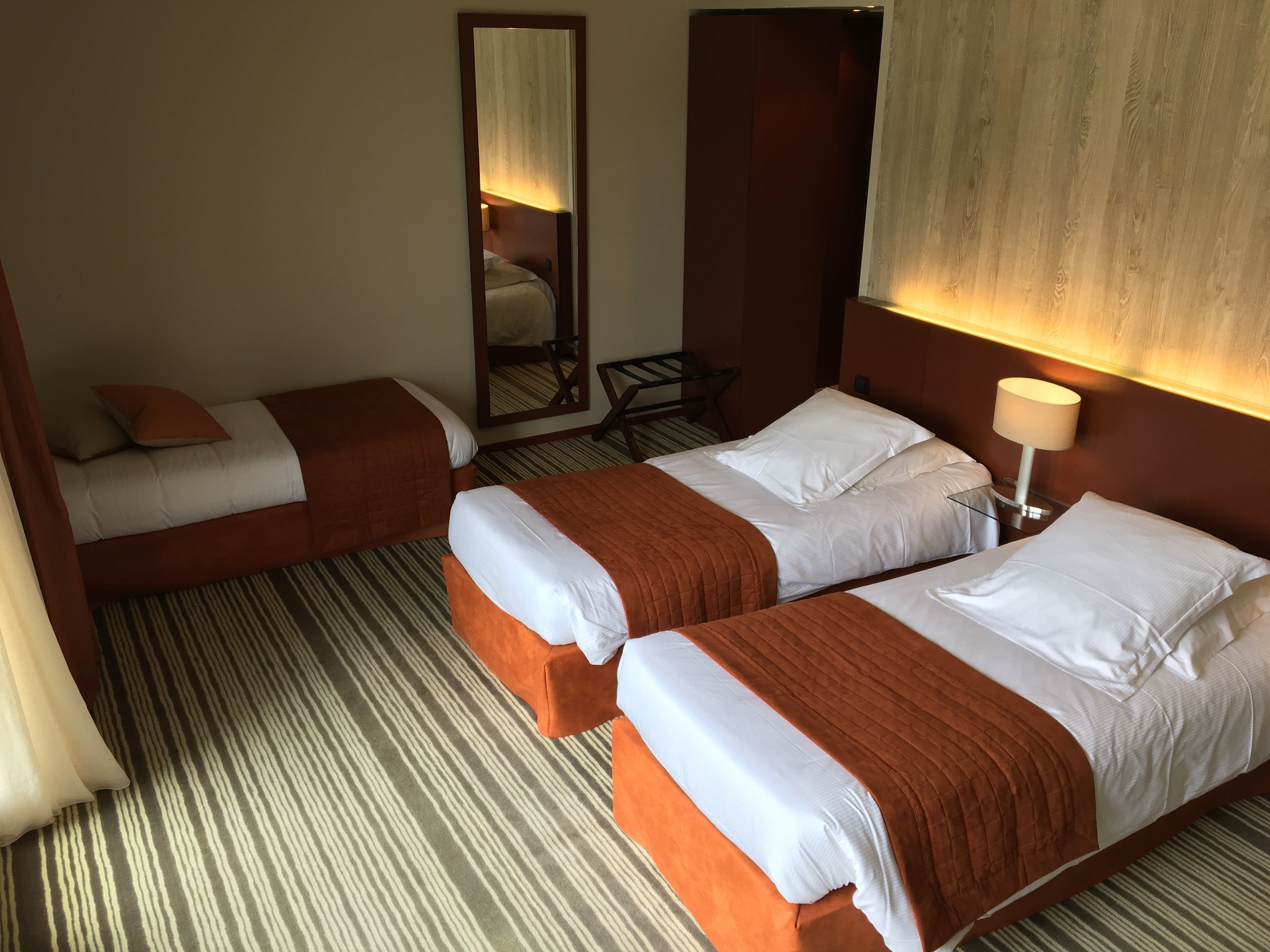 A hotel room with two beds, striped carpet, a mirror, and a lamp.