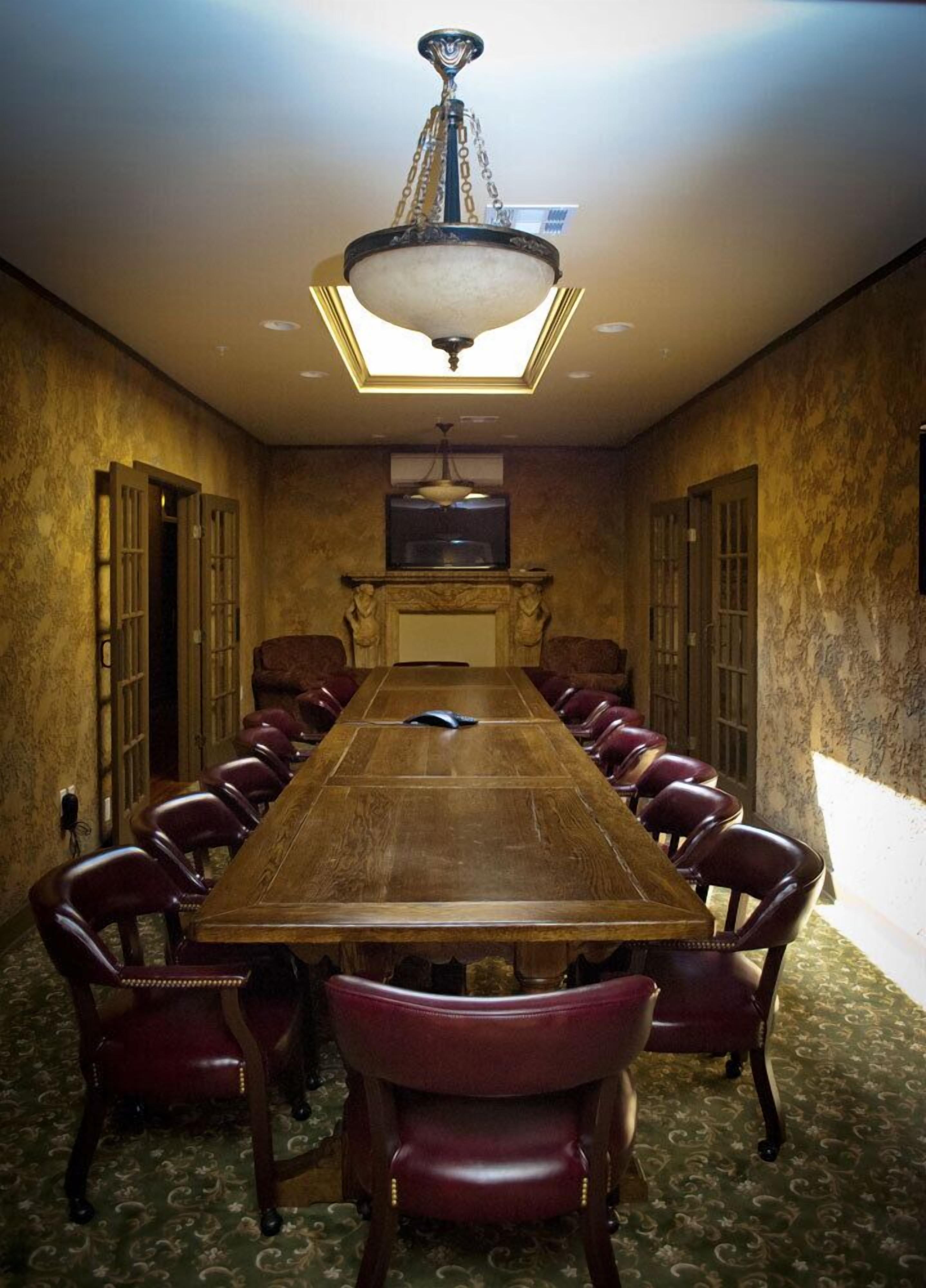 A conference room with a long wooden table, leather chairs, a chandelier, and a fireplace.