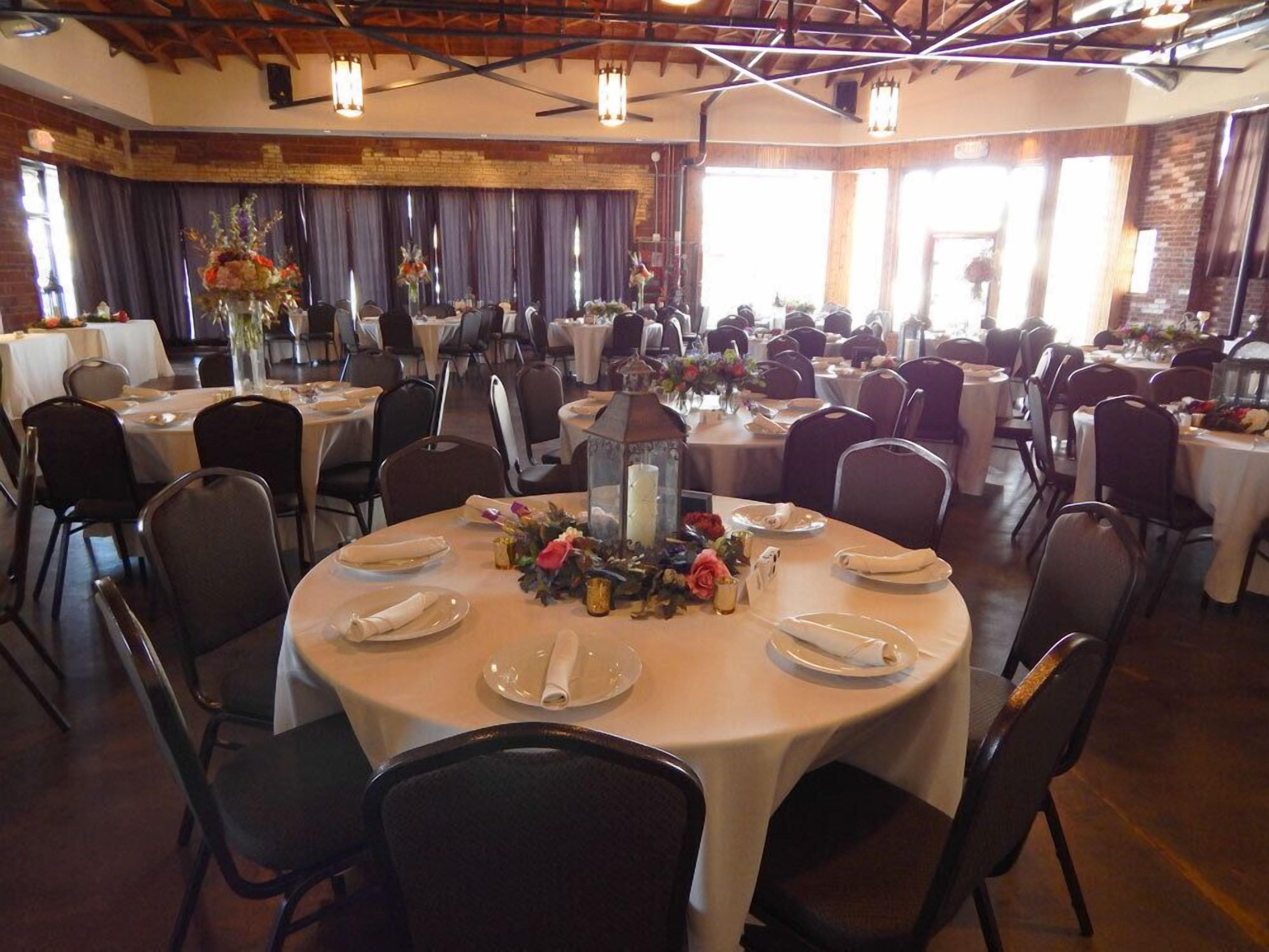 Un salón de banquetes con mesas redondas dispuestas para cenar, con centros de mesa y velas.