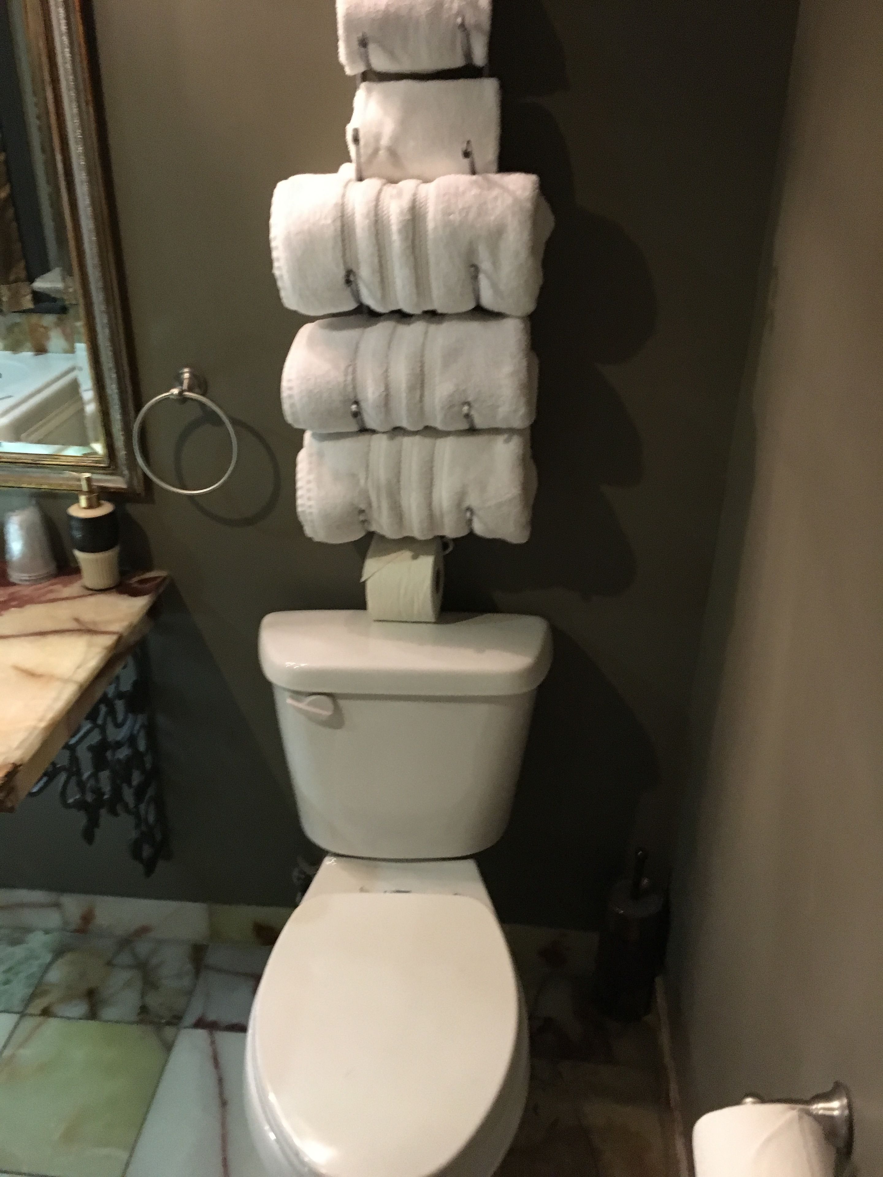 A toilet with a stack of white towels hanging on the wall beside it.