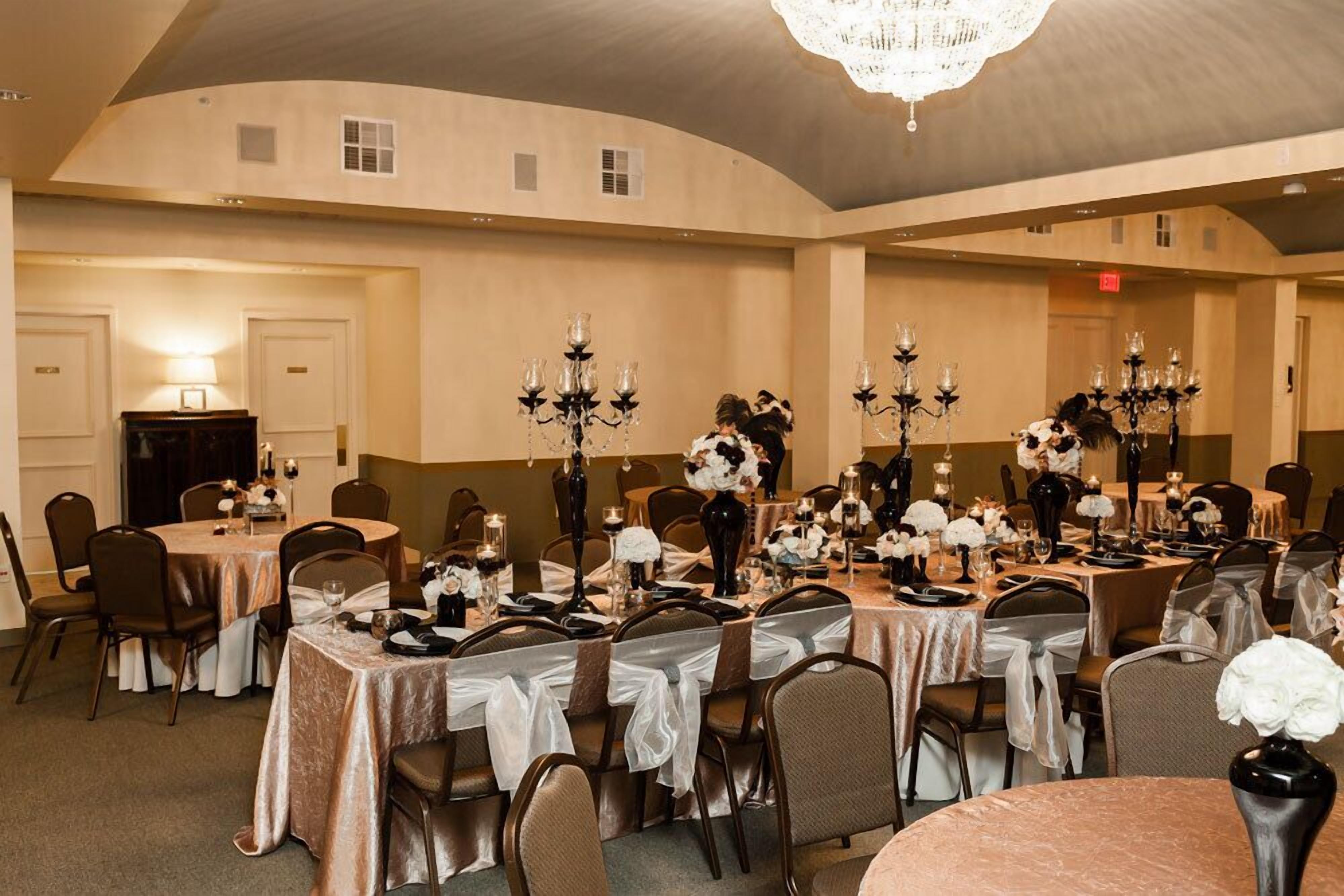 A banquet hall with round tables set for a formal event, featuring chandeliers and floral centerpieces.