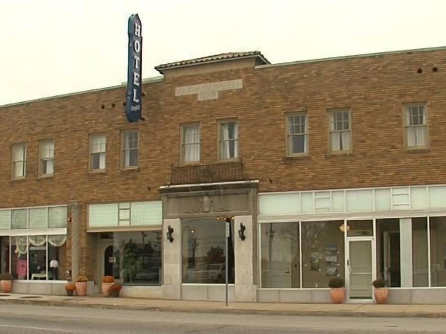 A two-story brick building with a sign reading "HOTEL" above the entrance. There are large windows on the ground floor and a smaller entrance with a door.