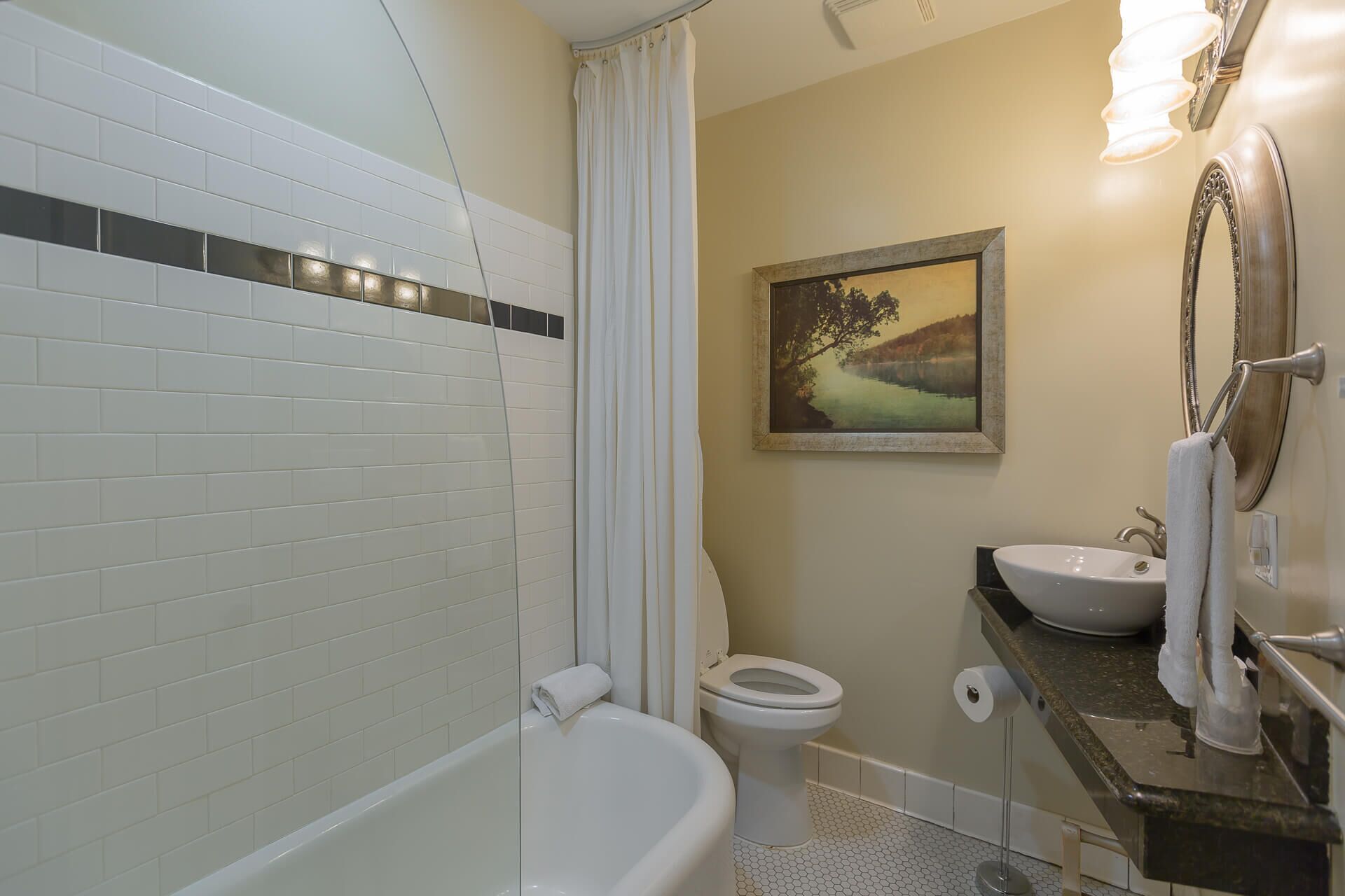 A bathroom with a bathtub, toilet, sink, and a painting on the wall.