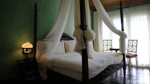 A four-poster canopy bed with white linens, a bedside table with a lamp, and a view of the room through sheer curtains. - Joaquin's Bed and Breakfast (Tagaytay)