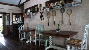 A dining area with wooden tables and chairs, a bar with bottles, and various decorative items on the wall. - Joaquin's Bed and Breakfast (Tagaytay)