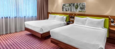 A hotel room with two beds, a large window with curtains, a wooden headboard, and a wall-mounted artwork.