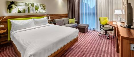 A hotel room with a large bed, a sofa, a desk, and a chair.