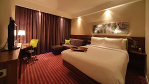 Habitación de hotel con una cama grande, un escritorio con ordenador, una silla, un sofá y televisor montado en la pared.