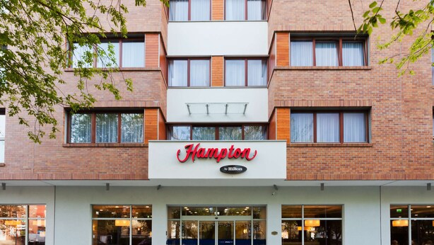 Un hotel Hampton by Hilton con fachada de ladrillo moderno, ventanas grandes y un letrero llamativo.