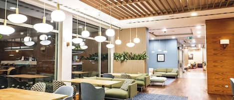 A modern office space with round tables, green sofas, and hanging pendant lights.