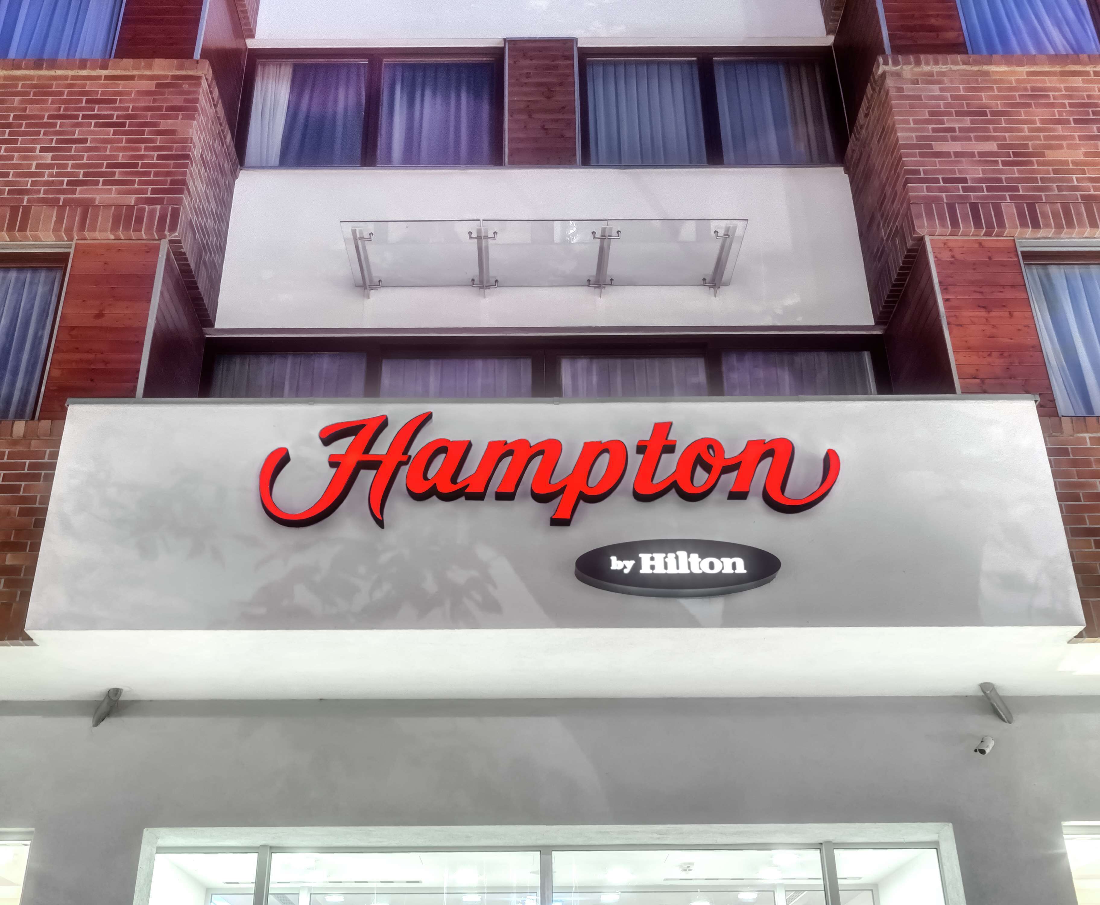 Ein Hotel-Schild mit der Aufschrift "Hampton by Hilton" in roter und schwarzer Schrift.