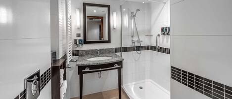 Un baño moderno con ducha envuelta en vidrio, tocador con lavamanos y un espejo grande.