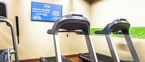 A gym area with treadmills and a sign for WYNAJEM ROWEROW.