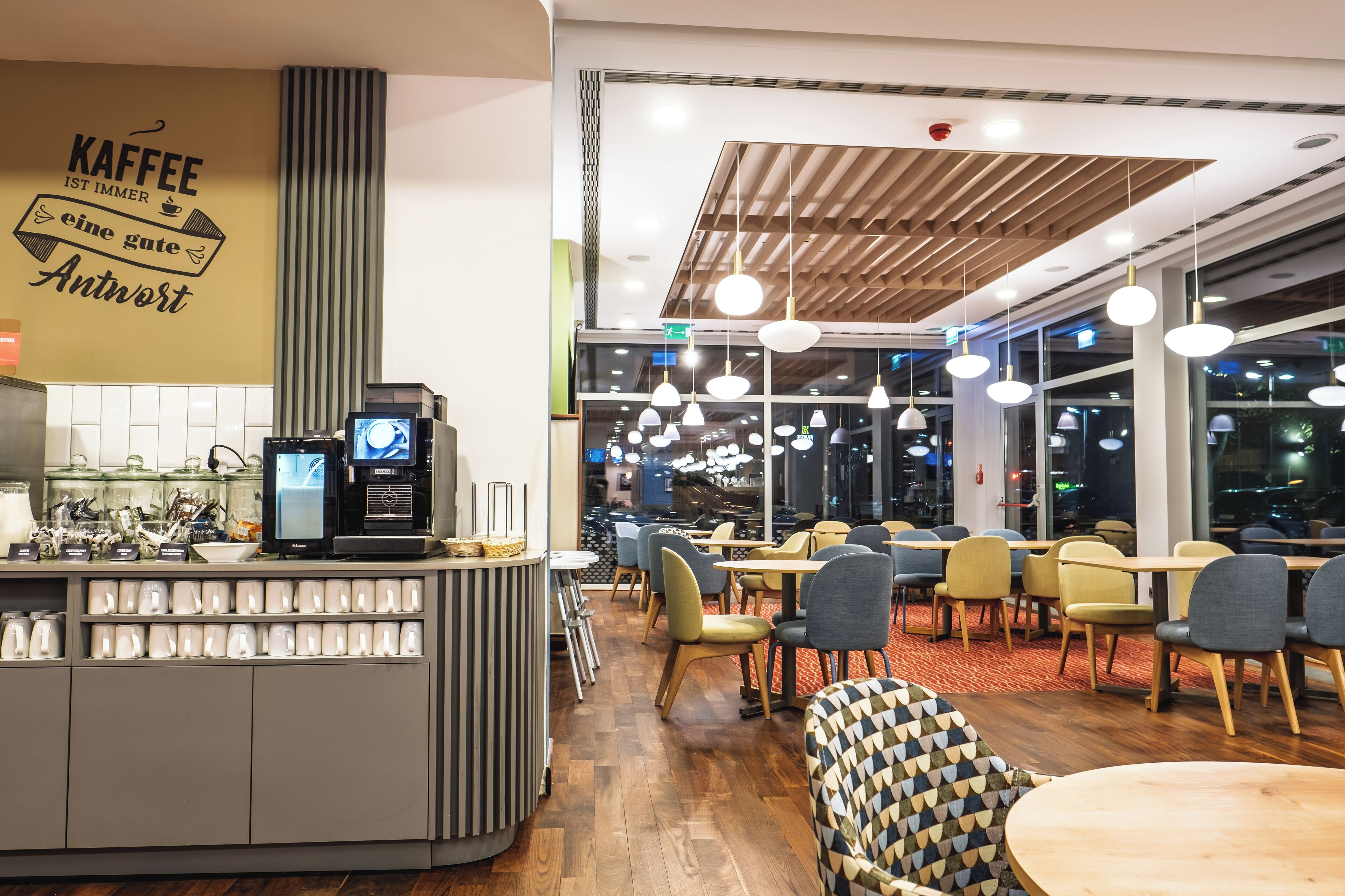 A modern coffee shop interior with a counter displaying coffee machines and a menu board, seating area with tables and chairs, and large windows offering a view of the cityscape.