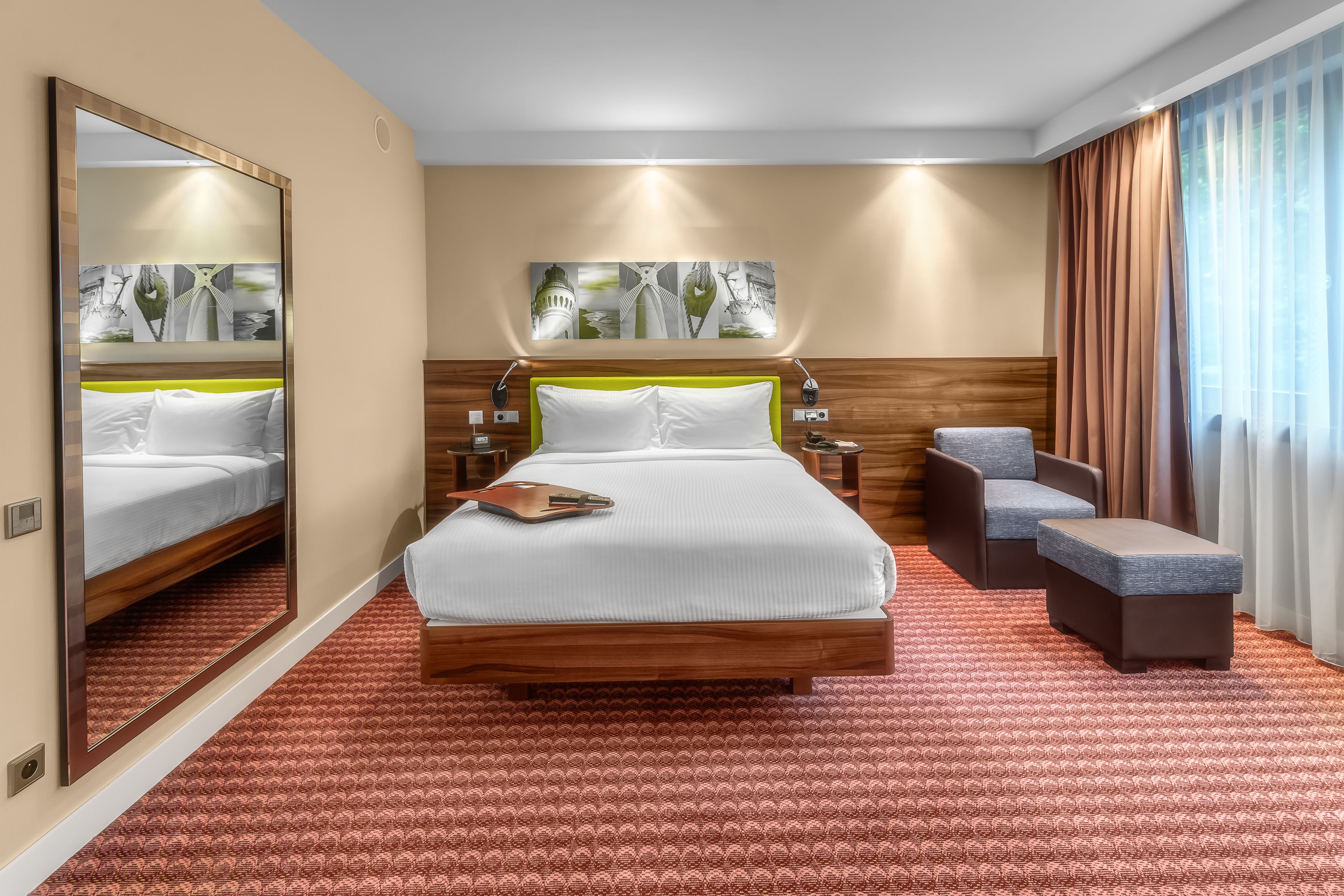 A hotel room with a large bed, a small sofa, a mirror, and artwork on the wall.