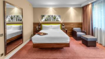 A hotel room with a large bed, a small sofa, a mirror, and artwork on the wall.