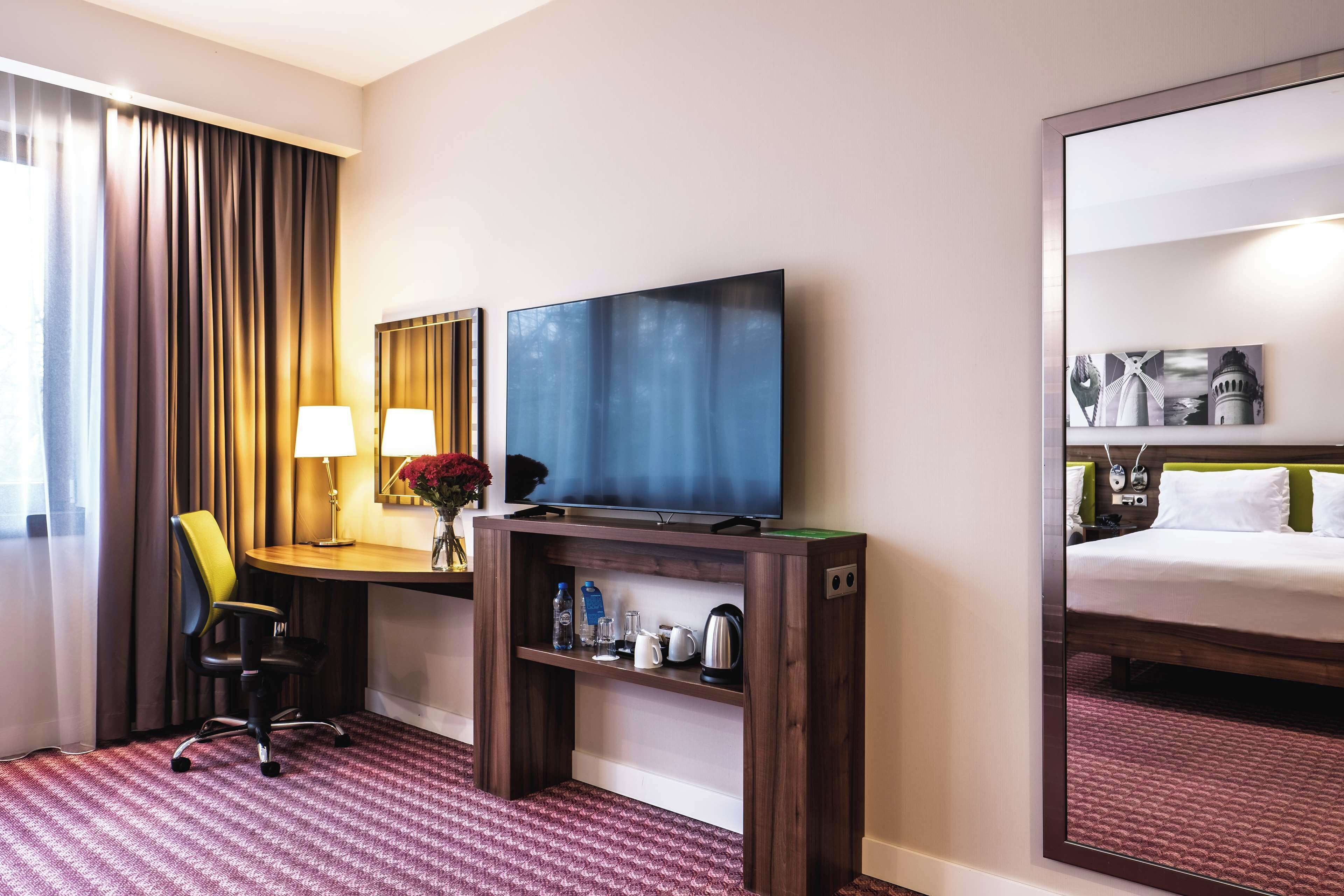 Ein Hotelzimmer mit einem Bett, einem Fernseher, einem Schreibtisch mit Stuhl, einer Kaffeemaschine und einem Spiegel.