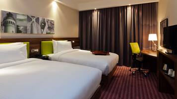 Ein Hotelzimmer mit zwei Betten, einem Schreibtisch, einem Stuhl, einem Fernseher und Bildern an der Wand.