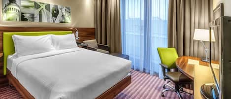A hotel room with a large bed, a desk, a chair, a TV, and a window with curtains.
