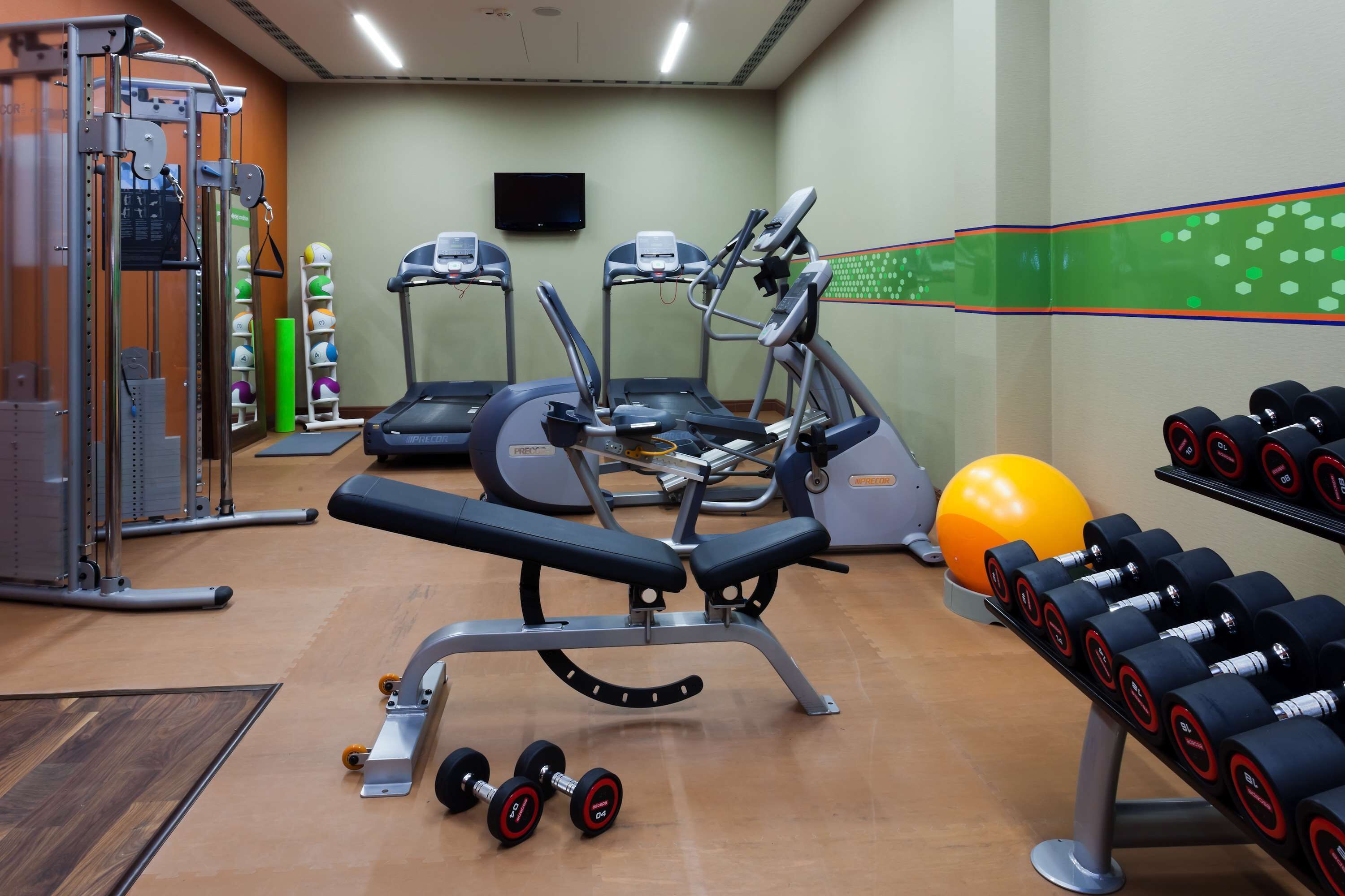 Ein Fitnessstudio mit Trainingsgeräten, Laufbändern, Kurzhanteln und einem großen Trainingsball.