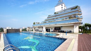 A swimming pool with a mermaid mural, a building with blue-tiled balconies, and a clear sky.