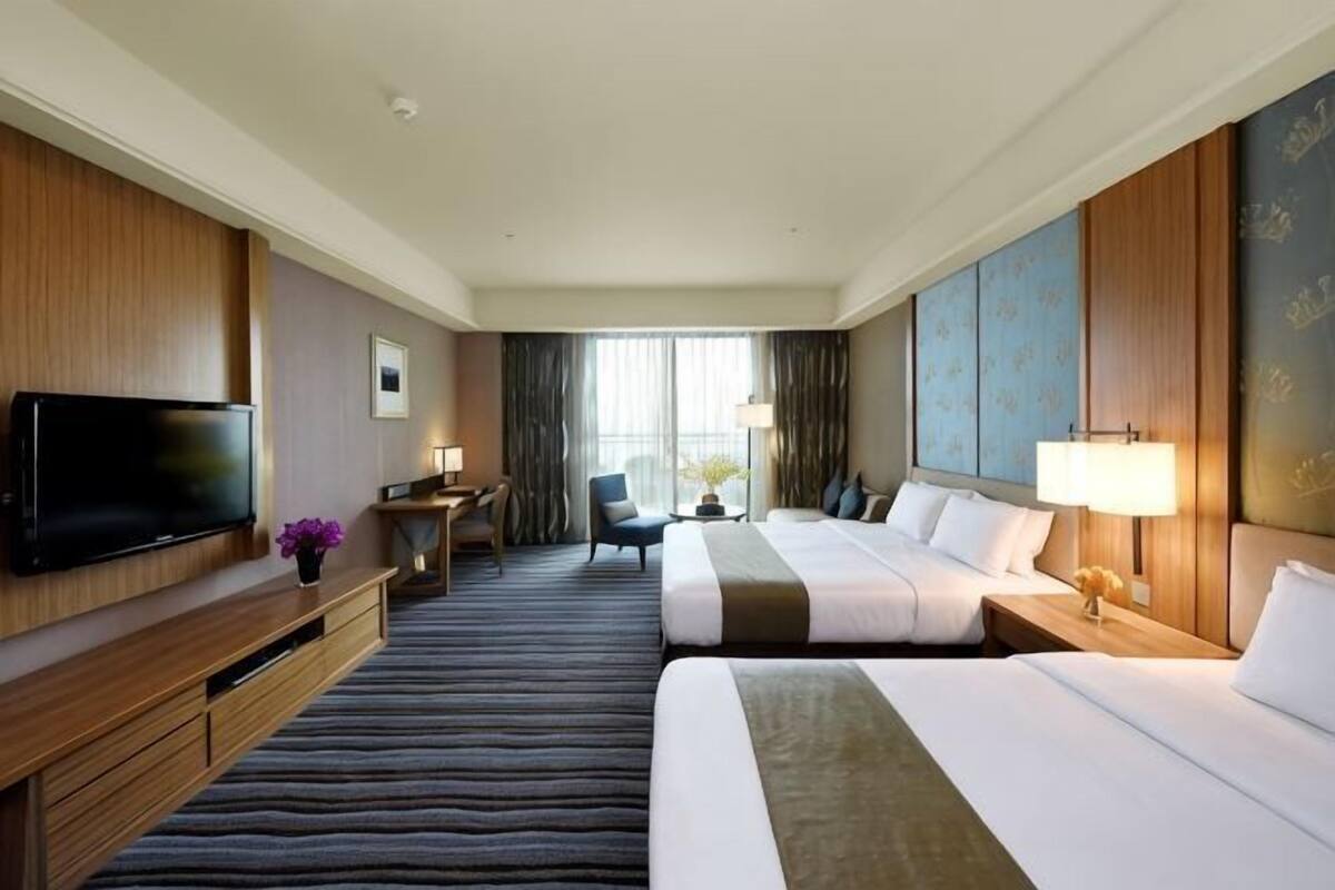 Habitación de hotel con dos camas, televisión, escritorio con lámpara y vistas a la ciudad.