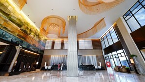 A spacious lobby with a high ceiling, modern chandeliers, and a large central column.